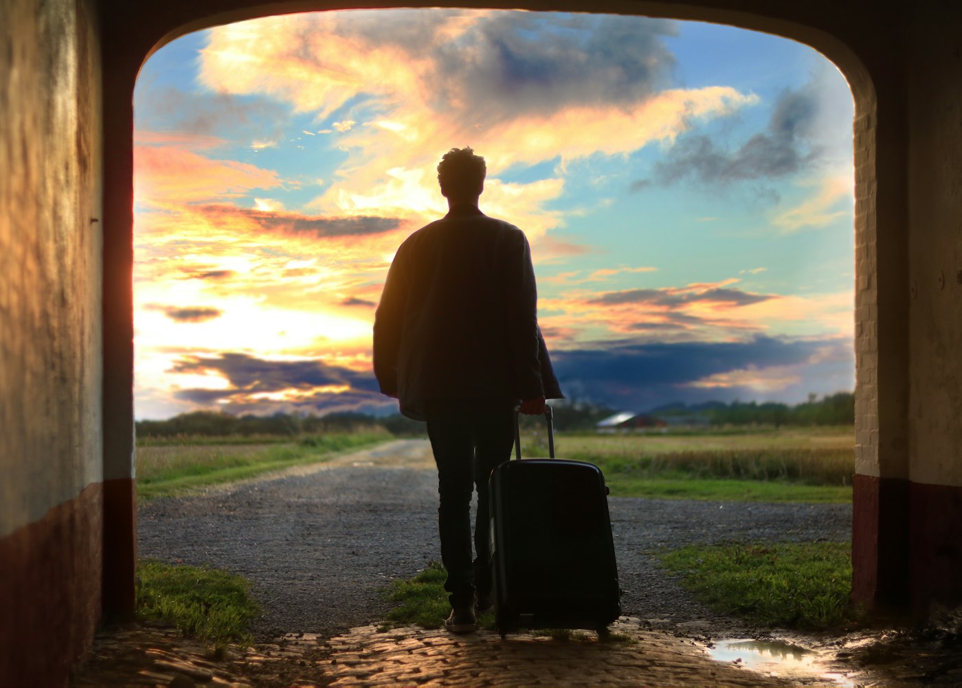 Viajante com mala caminhando em direção a um pôr do sol